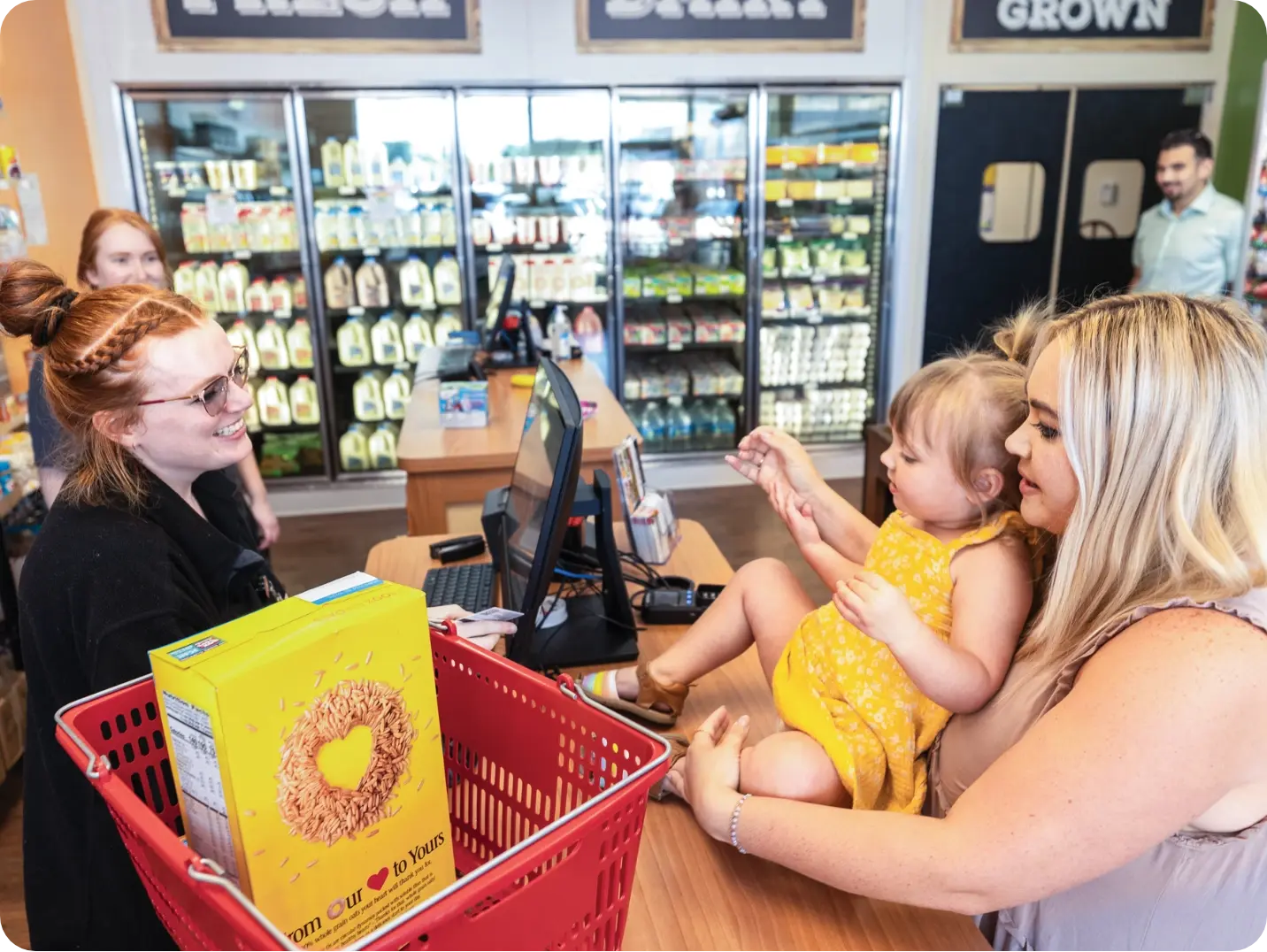 Mother holding child at grocery store checkout.