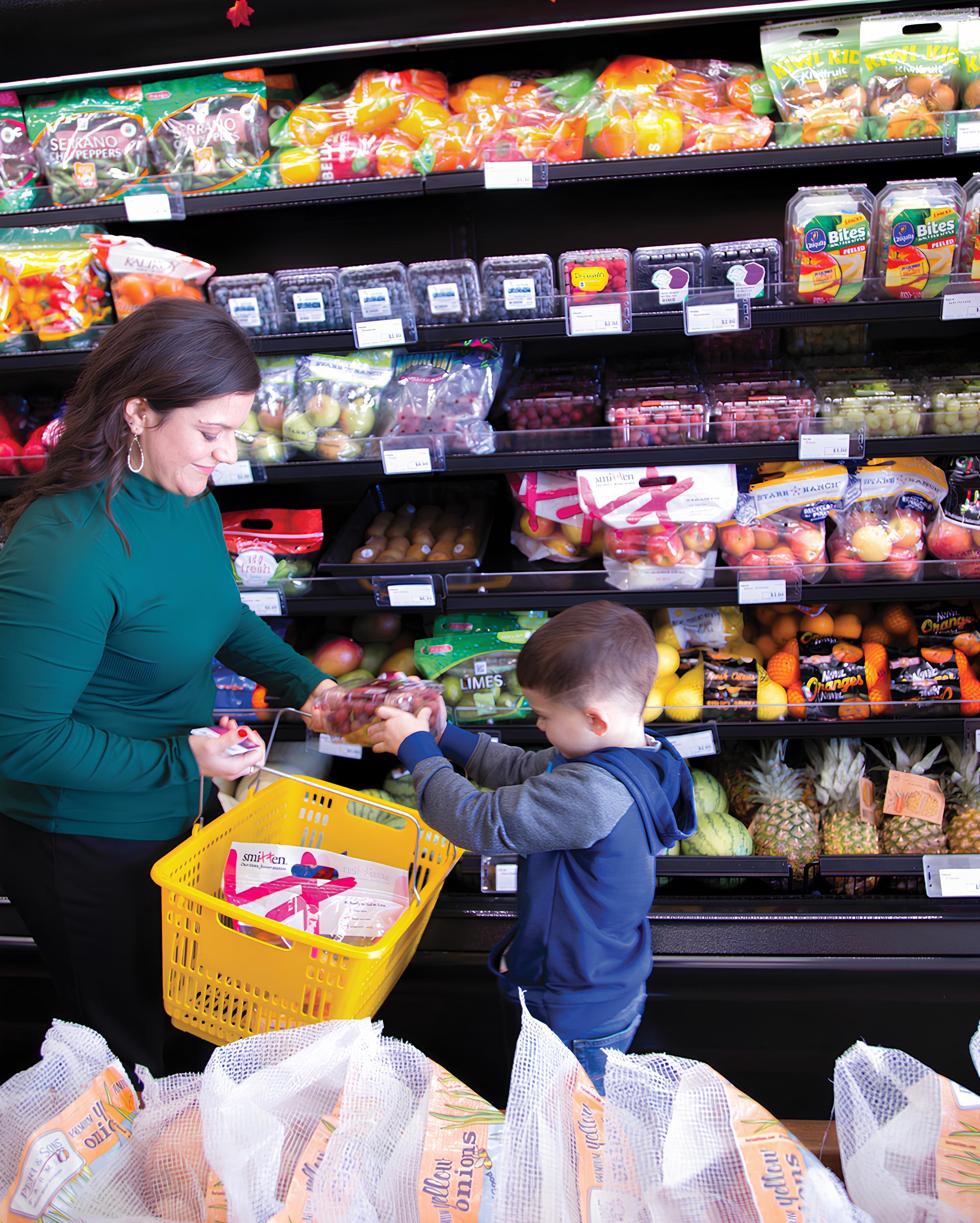 Child hands grapes to adult in grocery store.