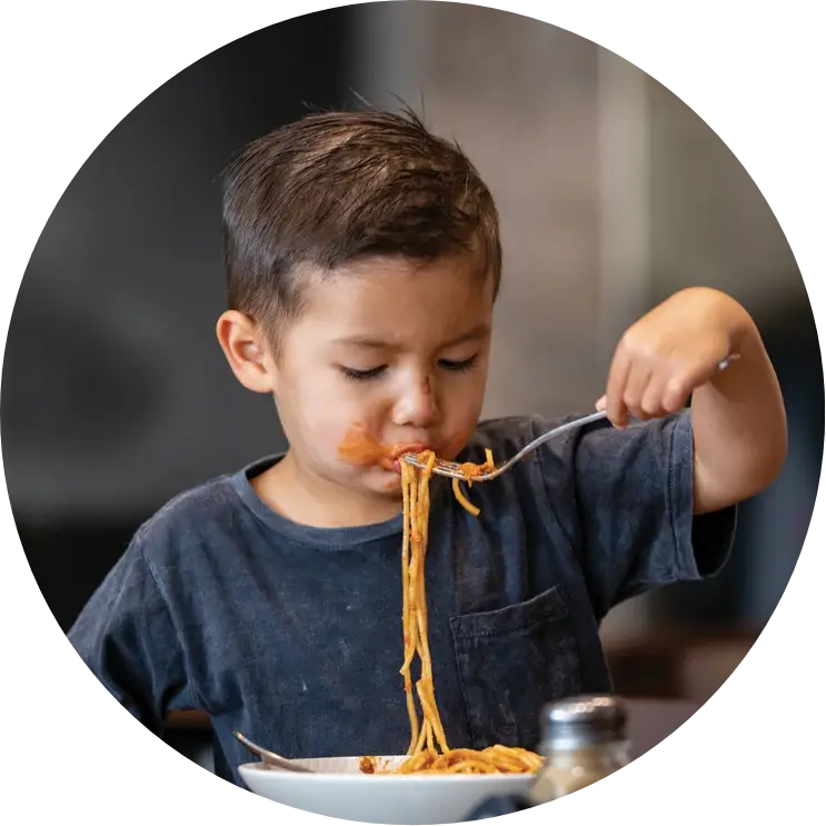 Child eating spaghetti with sauce, focused and messy.